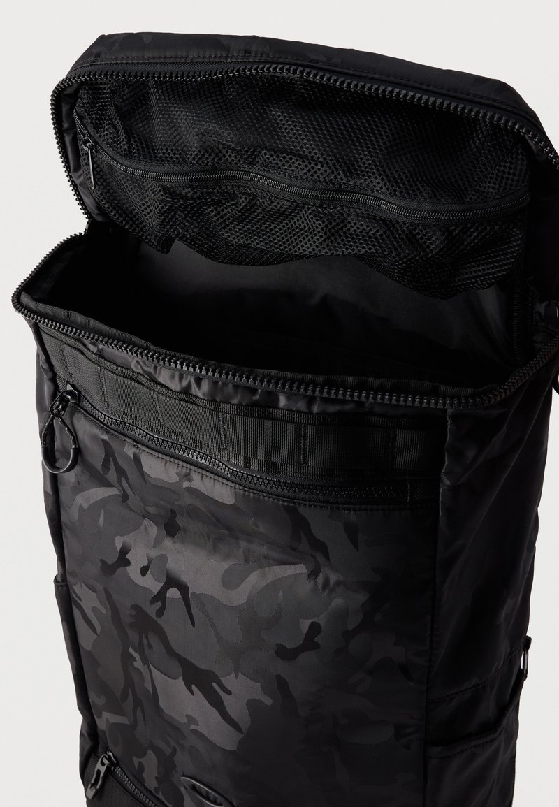 Zaino nero con motivo mimetico con scomparto superiore aperto che mostra una tasca interna in rete nera con zip.