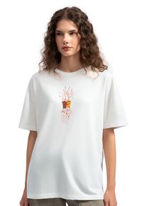 Witte katoenen t-shirt met een losse pasvorm, met een centraal grafisch ontwerp van een plant in een oranje pot, gedetailleerd met rode en roze accenten.