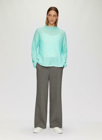 Un pull en tricot côtelé, ample, couleur bleu sarcelle clair, associé à un pantalon large taille haute gris et des baskets blanches. Fond uni.