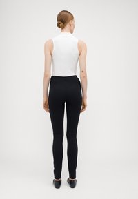 Hvit ærmeløs topp med høy hals, kombinert med svarte tettsittende bukser. Antrekket har en glatt tekstur og et enkelt design.