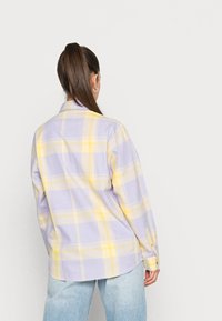 Langermet rutete skjorte i lavendel og gul, med knappelukking, mykt stoff og avrundet kant. Bært med lyseblå jeans.