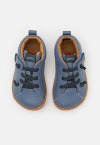 Scarpe in pelle blu con suole in gomma, dotate di lacci verde scuro e una cinghia laterale. L'interno ha una foderatura color tan.