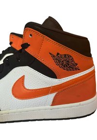 Sneaker alta con pannelli in pelle nera, bianca e arancione. Presenta un materiale texturizzato, lacci neri e un logo "Air Jordan" in rilievo.