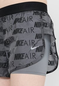 Grå träningstights med svart "NIKE AIR"-tryck, nätpaneler i sidorna och svart elastisk midja. Har en lagerdesign och en slät innersöm.