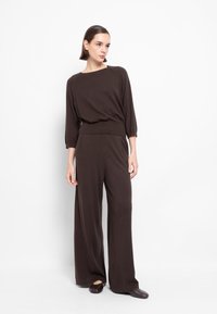 Salopette marrone lavorata a maglia con gambe larghe e top dal taglio rilassato, con scollatura a barca e maniche a tre quarti. Realizzata in tessuto morbido.