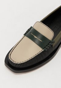 Mocassins en cuir avec une base noire, un devant beige et une bande d'accent verte. Couture texturée et design élégant à bout carré.