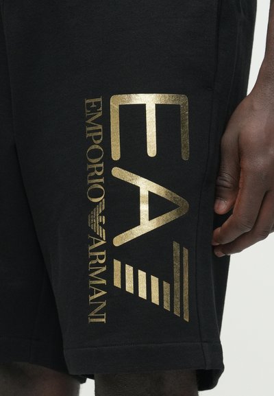 Черни къси панталони с метално златно лого "EA" и надпис "Emporio Armani", с хоризонтални райета отстрани. Изработени от памук, с удобна ежедневна кройка.