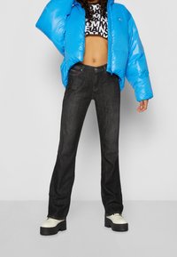 Blue puffer jacket, black straight-leg jeans, and chunky white platform shoes. The outfit features graphic print on a cropped top.