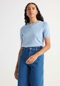 Lysblå strikket top med korte ærmer og rund hals, parret med højlivet mørke denim jeans. Blød tekstur, tætsiddende design.