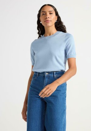 Lysblå strikket top med korte ærmer og rund hals, parret med højlivet mørke denim jeans. Blød tekstur, tætsiddende design.