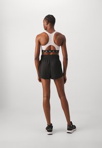Sports bra with a racerback design in light color, paired with black shorts featuring an elastic waistband and branded accents.