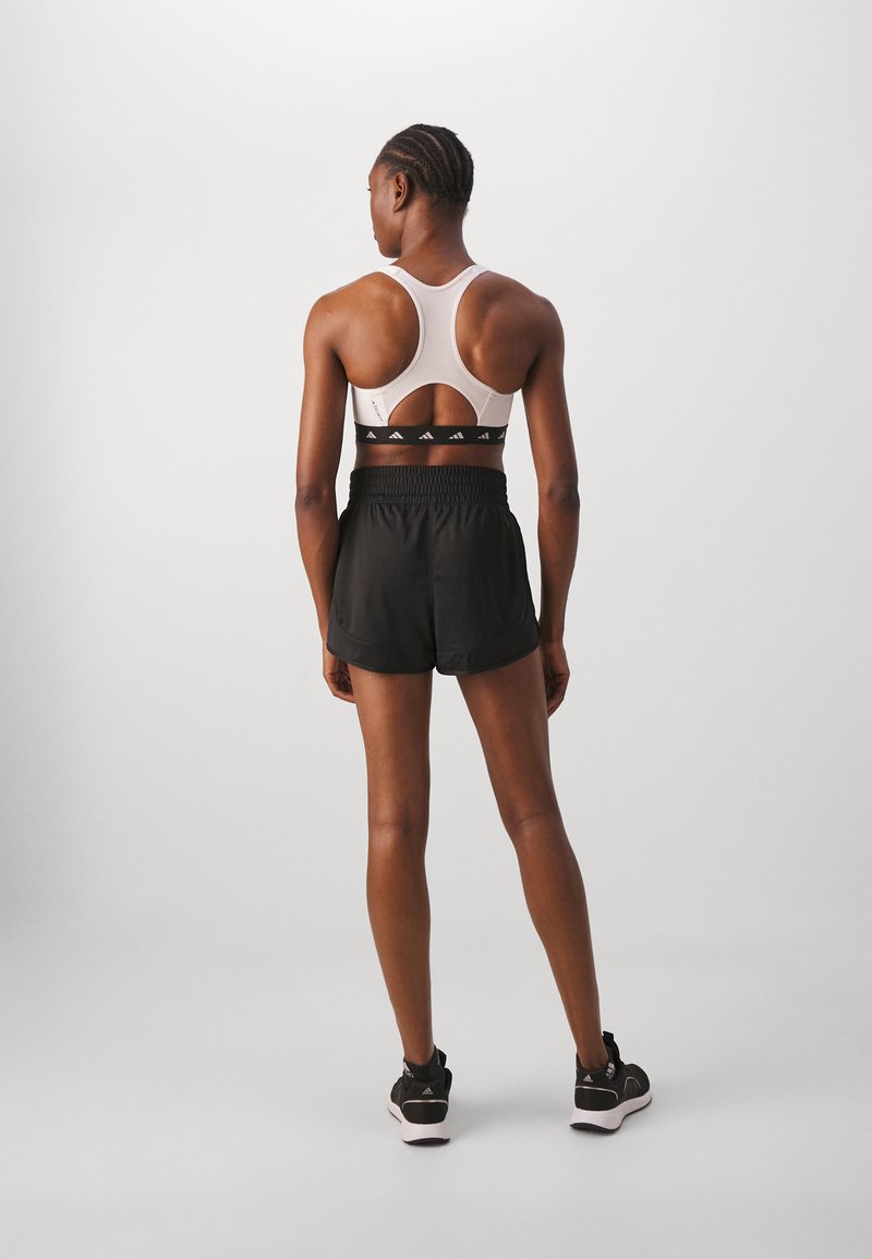 Sujetador deportivo con un diseño de espalda cruzada en un color claro, combinado con pantalones cortos negros que tienen una cintura elástica y detalles de marca.