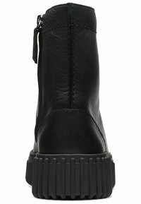 Botín negro de cuero con suela de goma acanalada, que incluye un zipper lateral y detalles de costura en la parte trasera y los lados.