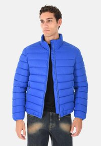 Giacca a vento blu con colletto corto, design trapuntato, chiusura zip, due tasche laterali e una texture liscia e lucida.