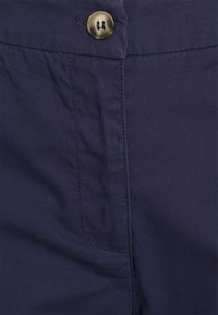 Tissu en coton bleu marine avec une surface texturée, doté d'une fermeture à deux boutons et de détails de poches latérales. Couture soignée visible.