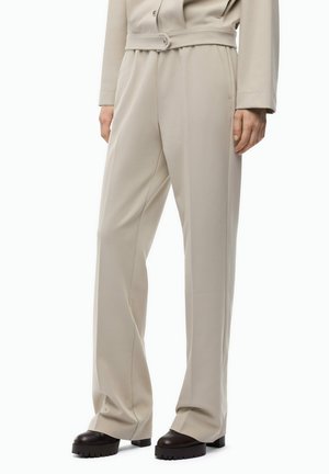 Pantaloni beige a gamba larga abbinati a scarpe nere con suola spessa, mostrati su una persona in piedi dalla vita ai piedi.