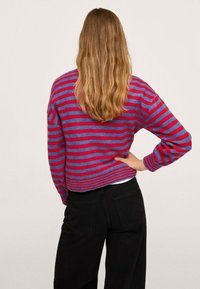 Suéter a rayas rojas y azules con un corte relajado y mangas largas, que presenta puños y dobladillo acanalados, combinado con pantalones negros.