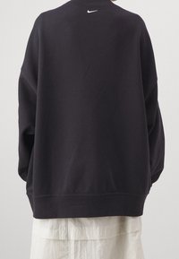 Felpa nera oversize con collo a giro, maniche lunghe e logo Nike bianco sulla parte superiore della schiena. Materiale in cotone liscio.
