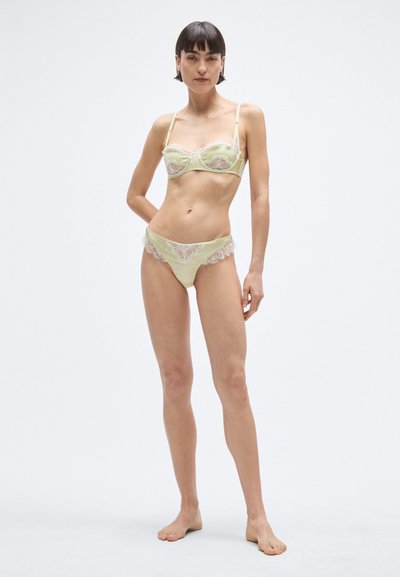 Világoszöld szatén fehérnemű szett, amely balconette típusú melltartót tartalmaz csipke szegéllyel és hozzá illő, csipke díszítésű alsóneműt. Áttetsző textúrájú részletek.