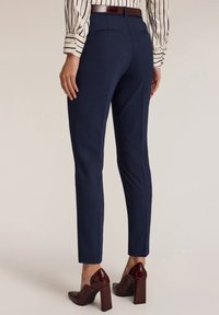 Námořnické modré kalhoty na míru se slim fit, hladkým povrchem a zadními kapsami, doplněné lesklými vínovými botami na blokovém podpatku.