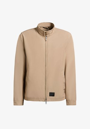 Beige herrejakke med opretstående krave, forlynlås, lukning med to knapper, sidelommer og sort rektangulært logopatch nær kanten.