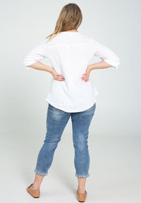 Haut en lin blanc à manches trois-quarts, ourlet arrondi, associé à un pantalon en denim bleu clair avec poignets brodés. Chaussures marron à enfiler.