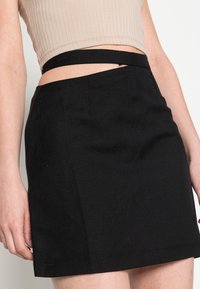 Gonna mini nera con un design aderente, realizzata in tessuto testurizzato. Presenta una vita alta e un dettaglio a taglio, che mette in risalto una silhouette moderna.