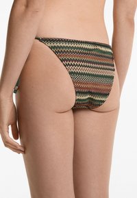 Costume da bagno con motivo a zigzag in tonalità terrose di verde, marrone e beige. Presenta sottili spalline e un design con copertura posteriore minima.