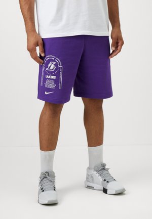 Lilla Nike shorts med Los Angeles Lakers branding, herunder tekst og logo. Båret med grå sneakers og hvide sokker.