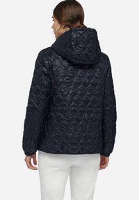 Veste matelassée marine avec capuche, présentant un motif en diamant texturé et des poignets élastiques. La vue arrière montre un design à coupe droite.