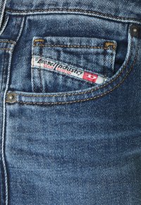Jeans aus Denim mit einer klassischen blauen Waschung, Kupfernähten, einer Münztasche und einem sichtbaren Etikett mit der Aufschrift "Diesel Industry Denim Division."