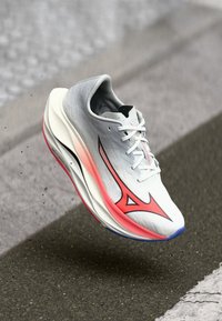 Scarpa da corsa con tomaia in rete grigio chiaro, dettagli rosa e un design elegante. Presenta una forma aerodinamica e una suola bianca ammortizzata.