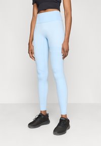 Ανοιχτό μπλε ψηλόμεσες κολάν από ελαστικό ύφασμα, με επίπεδες ραφές και ρίγες στα πλάγια. Συνδυασμένα με μαύρα αθλητικά παπούτσια.