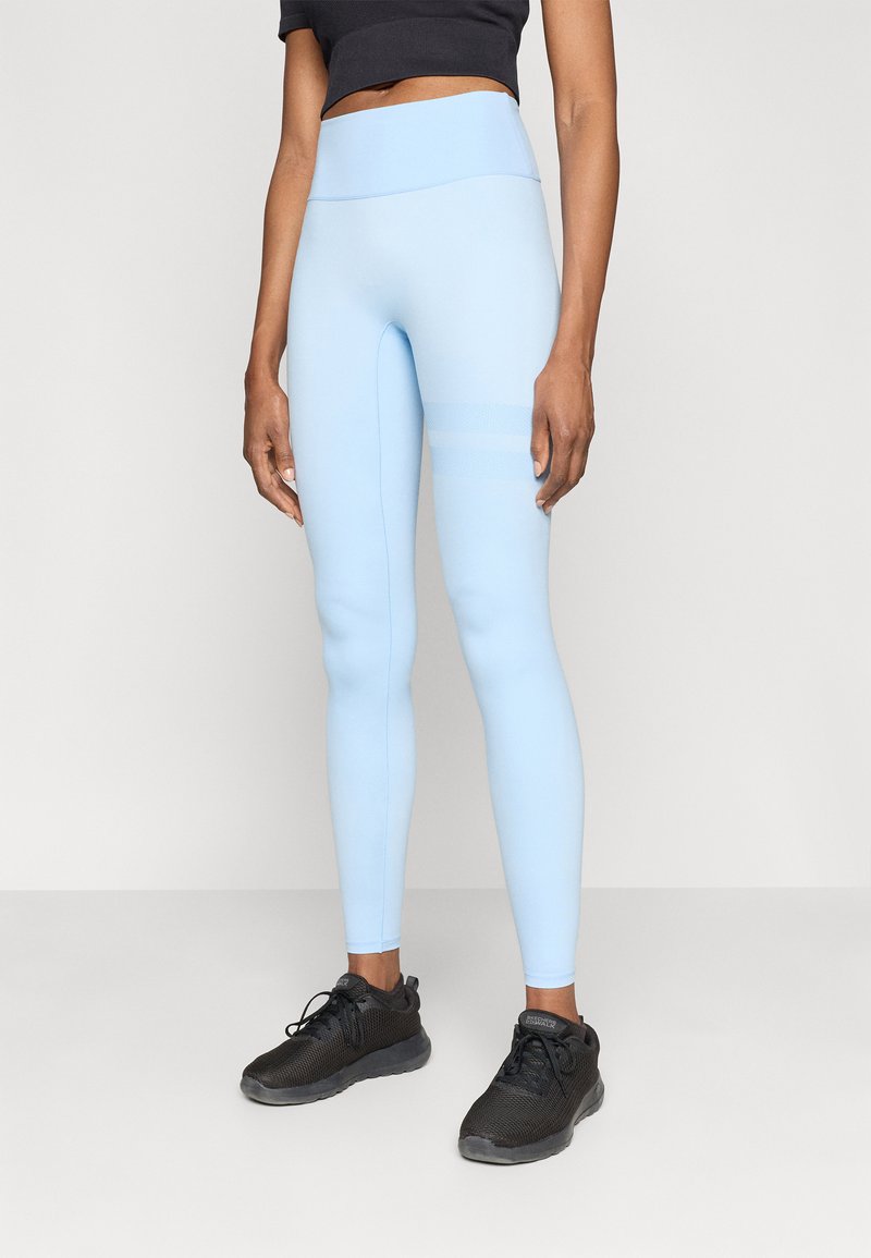 Ανοιχτό μπλε ψηλόμεσες κολάν από ελαστικό ύφασμα, με επίπεδες ραφές και ρίγες στα πλάγια. Συνδυασμένα με μαύρα αθλητικά παπούτσια.