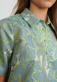 Kortärmad skjorta i ljusblå satin med ett blommönster i gult och grönt samt en spetsig krage.