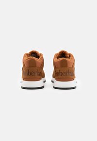 Botas de tobillo marrones con un acabado texturizado, que cuentan con un forro suave, una entresuela blanca y el logo de "Timberland" en el talón.