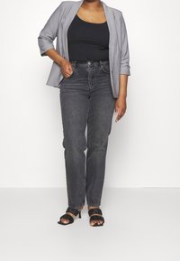 Grauer Blazer über einem schwarzen Top, kombiniert mit hoch taillierten dunkelgrauen Jeans und schwarzen Riemchenheels. Hat eine schmale Passform und glatte Texturen.