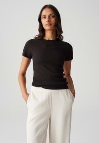 Top corto a maniche corte nero in maglia con scollo rotondo, design aderente e texture liscia, indossato con pantaloni larghi color crema.