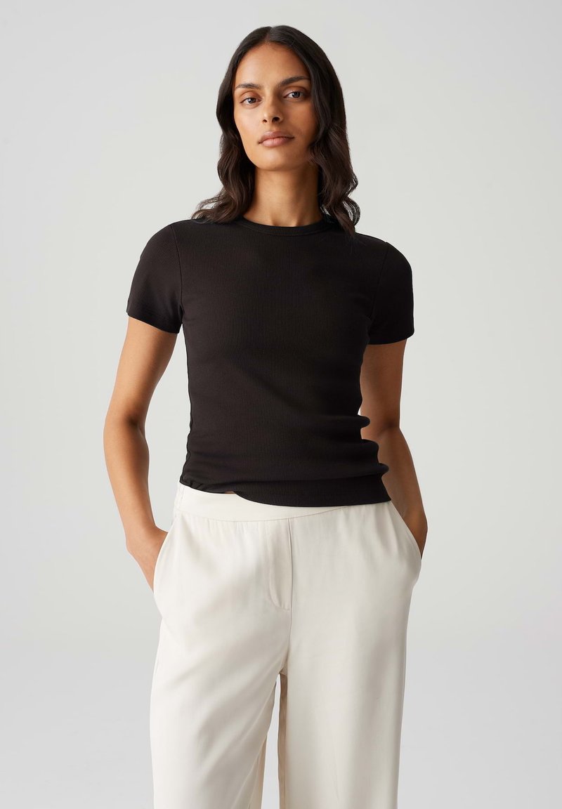 Top corto a maniche corte nero in maglia con scollo rotondo, design aderente e texture liscia, indossato con pantaloni larghi color crema.