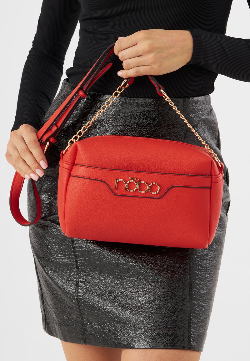 Borsa in finta pelle rossa con texture e ferramenta dorata, caratterizzata da un logo e dettagli con catena. Tracolla regolabile per versatilità.