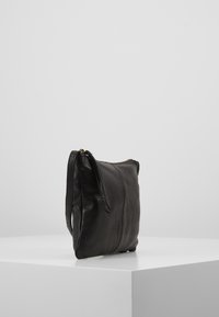 Borsa a mano in pelle nera con una texture liscia, chiusura con zip e manico laterale. Forma rettangolare con dettagli di cuciture minimaliste.