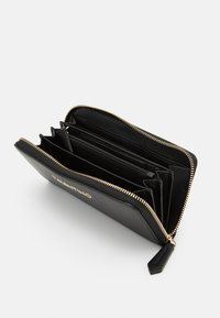 Črn usnjen denarnica z zlatim zadrgo, več predelki, notranji režitelji za kartice in teksturirana površina. Logotip blagovne znamke je vtisnjen na zunanji strani.