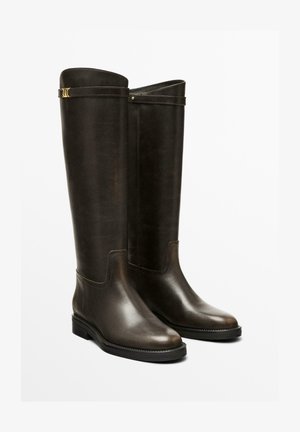Bottes en cuir marron montantes avec une texture lisse, bout rond, petit talon carré et accents en métal doré près du haut.