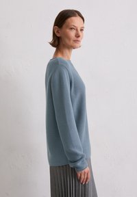 Jasnoniebieski sweter z prążkowanego dzianiny z długimi rękawami i okrągłym dekoltem, zestawiony z plisowaną szaro-skalą spódnicą. Gładka faktura i luźny krój.