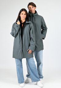 Vestes imperméables grises avec capuches, dotées d'une fermeture éclair à l'avant et de poches latérales, portées sur des hauts noirs, associées à des jeans bleu clair.