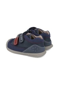 Bottines pour enfants en suède bleu avec une semelle en caoutchouc grise, dotées d'une sangle Velcro rouge, de coutures contrastées et d'un logo sur le talon.