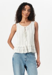 Lehký krémový peplum top se svislými béžovými pruhy, výstřihem ve tvaru lodi a mašlí na přední straně. Kombinovaný s modrými džíny s vysokým pasem.