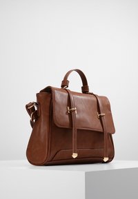 Ruskea nahkainen olkalaukku, jossa on jämäkkä muotoilu, kultaiset yksityiskohdat, ylhäältä kantohihna ja kaksi etuolkaa. Silkkinen pinta ja minimalistinen muotoilu.