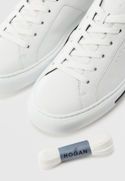 Pair of white leather sneakers with white laces and an extra bundle of white laces labeled "Hogan" on a white background.