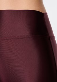 Bordowe legginsy sportowe z gładkiego, teksturowanego materiału. Posiadają wysoki pas z płaskimi szwami, co zapewnia komfort i elastyczność.